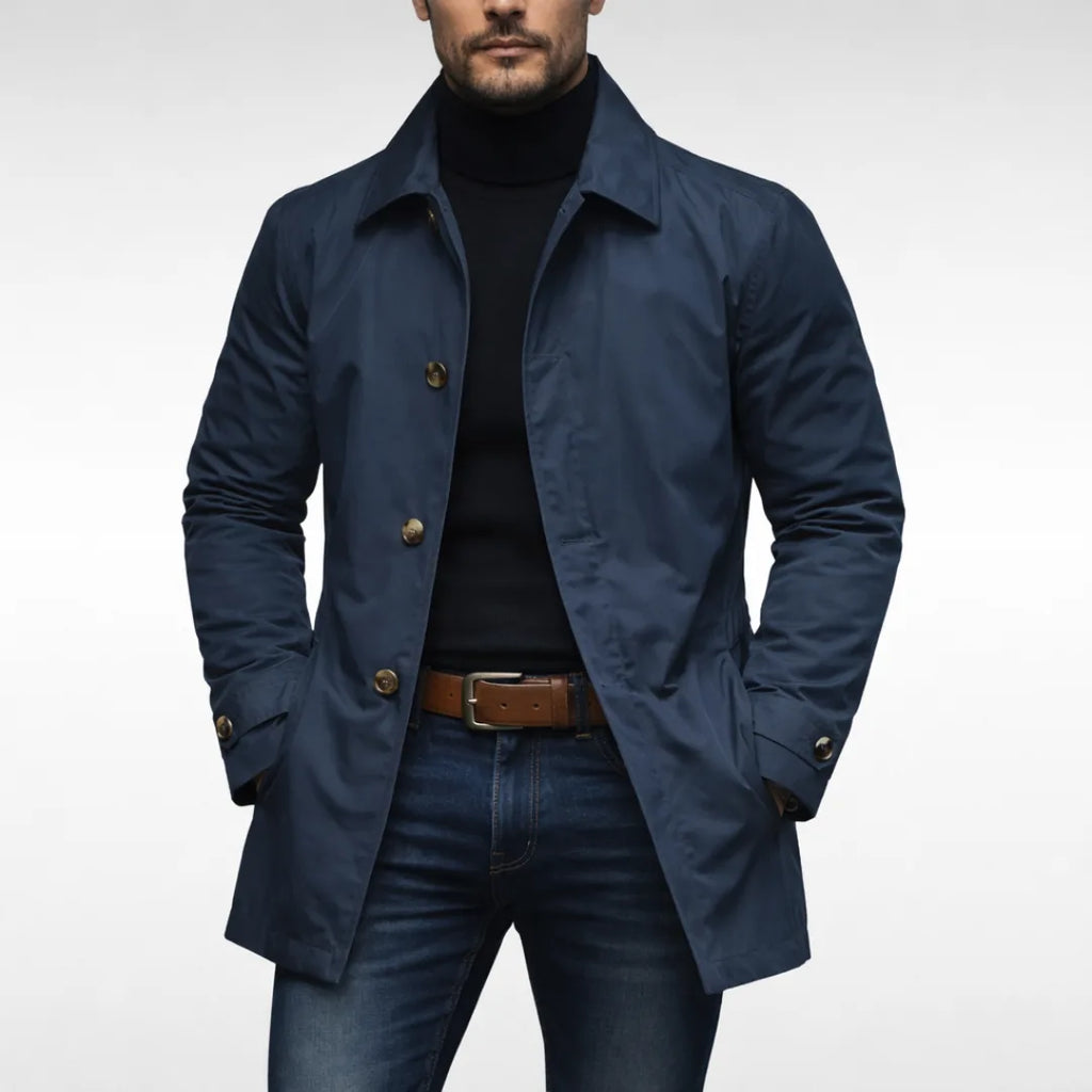 Man wearing a navy blue trench coat buttoned over a black polo neck, paired with a brown leather belt
