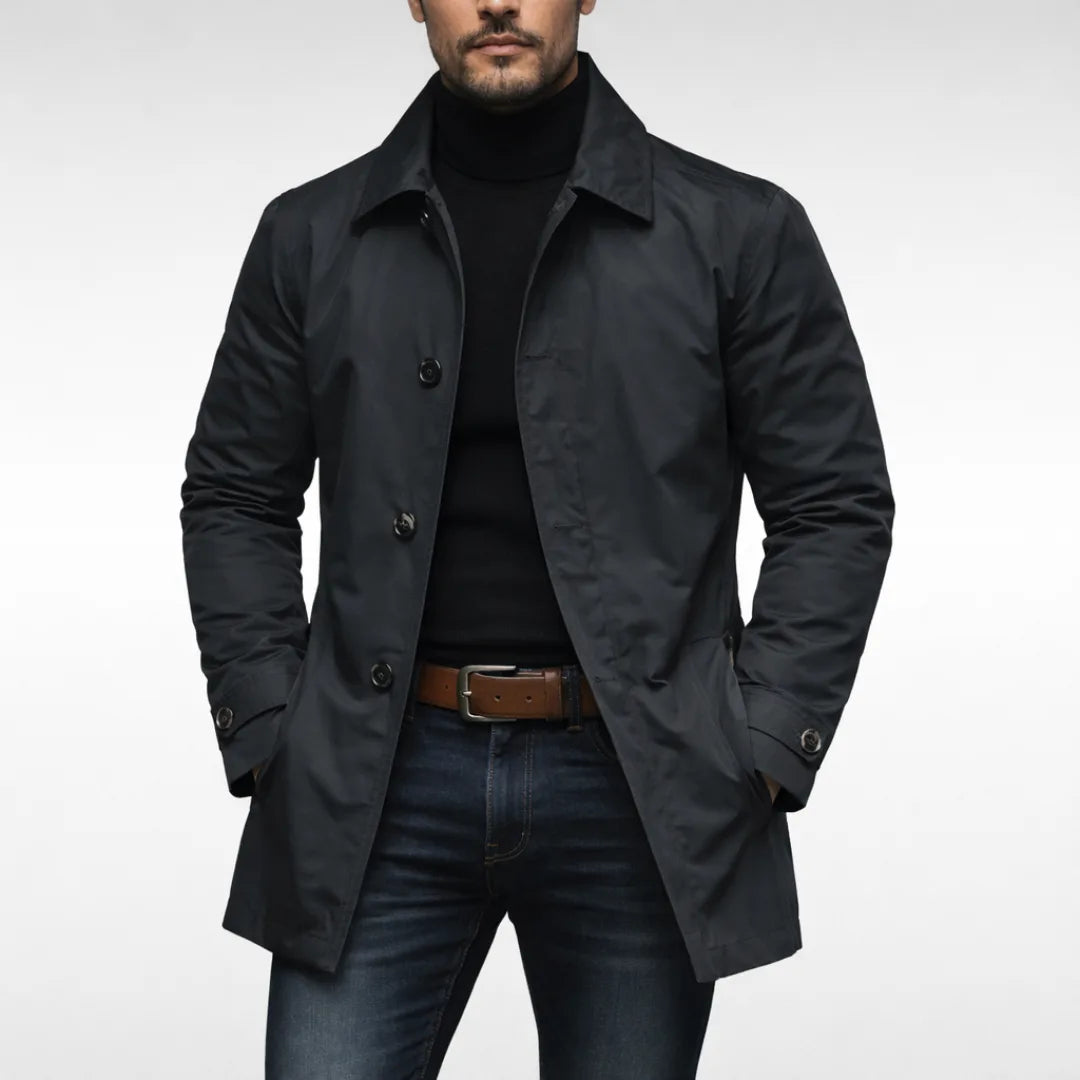 Man wearing a black trench coat open at the front, worn over a black polo neck and dark jeans