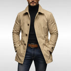 Man wearing a beige trench coat open over a black polo neck, paired with dark denim jeans