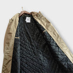 Interior view of a beige trench coat hanging open, showing the black quilted lining and inner pocket