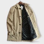 Side view of a beige trench coat on a wooden hanger, showing the black diamond-quilted inner lining
