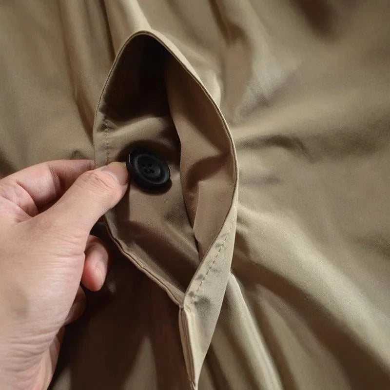 Close-up of a hand opening the welt pocket on a beige trench coat to show a black horn-style button