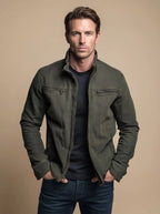 Man wearing an olive green cotton jacket with stand collar, zip-up front and two chest zip pockets, hands in side pockets