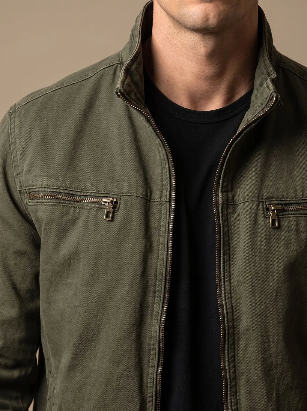 Close-up of the olive green jacket's stand collar, zip pull and chest pocket stitching detail