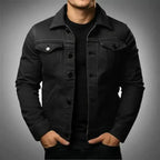 Man wearing a black denim trucker jacket fully buttoned over a black t-shirt, front view close up