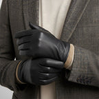 Close-up of a man in a tweed blazer wearing black leather gloves, hands clasped together at chest height