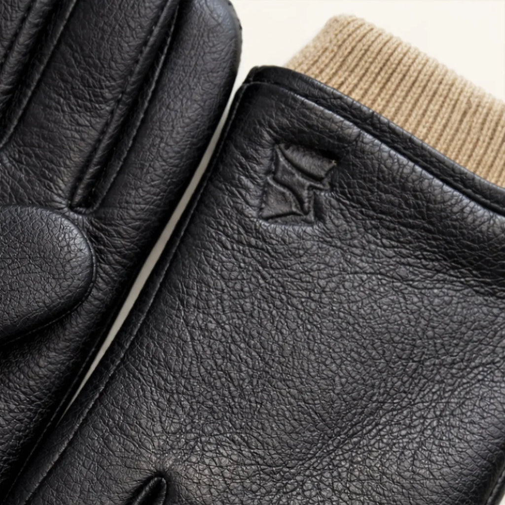 Close-up of the beige knitted cuff meeting black leather, with a small embossed logo on the glove wrist