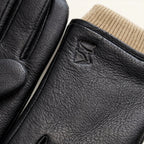 Close-up of the beige knitted cuff meeting black leather, with a small embossed logo on the glove wrist