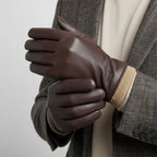 Man in a tweed blazer wearing brown leather gloves, hands clasped together over a cream jumper