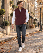 Man in a burgundy fleece gilet with full zip and stand collar, worn over a white top with jeans on a cobbled street