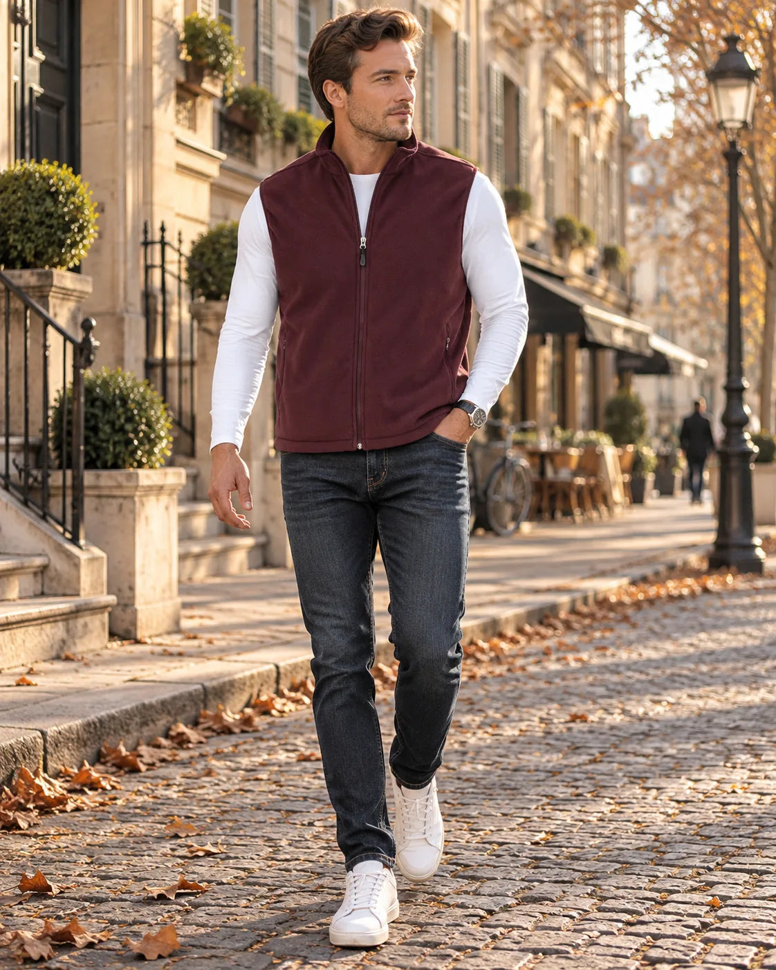 Man in a burgundy fleece gilet with full zip and stand collar, worn over a white top with jeans on a cobbled street