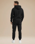 Back view of the black tracksuit showing the hood shape and ribbed cuffs