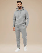 Man modelling a light grey hoodie and jogger tracksuit, front view with hands in pockets