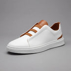 Angled studio shot of a white leather slip-on trainer with tan heel panel and elasticated loop laces