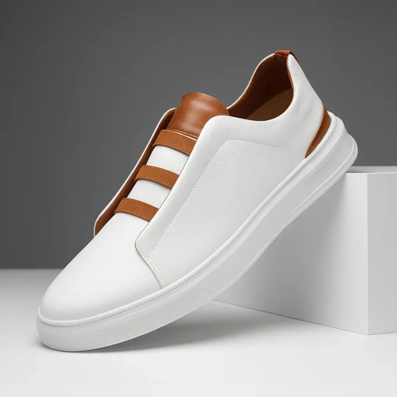 Three-quarter view of a white leather slip-on trainer with tan accents resting against a white block
