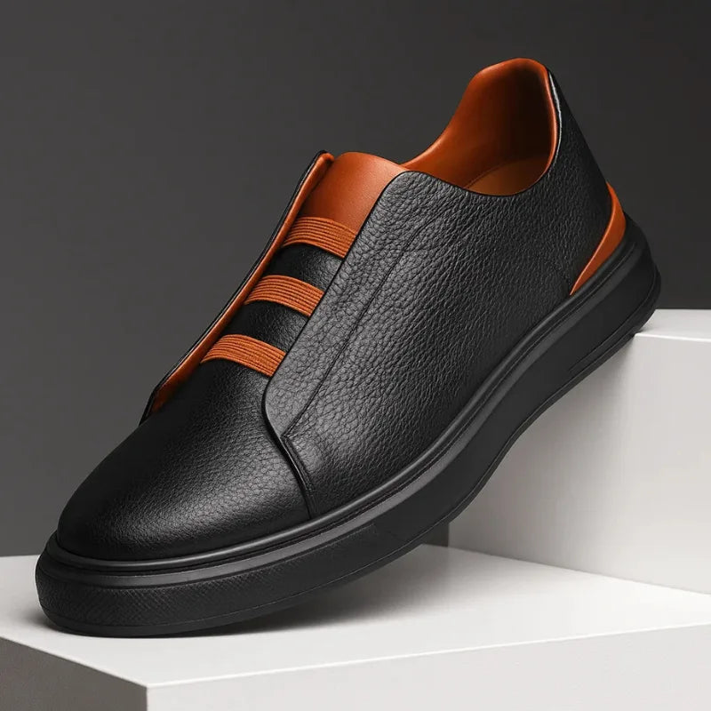 Three-quarter view of a black leather slip-on trainer with tan heel panel and tan loop laces