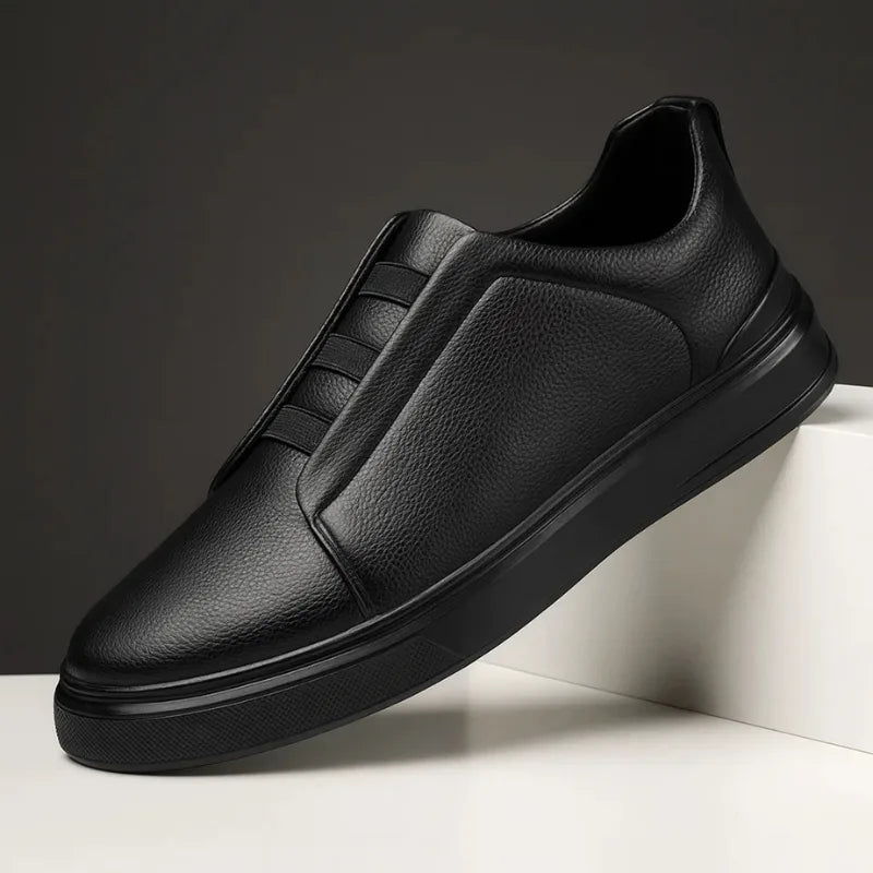 Side view of an all-black leather slip-on trainer with stitched panel detailing and black sole