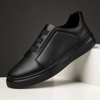 Side view of an all-black leather slip-on trainer with stitched panel detailing and black sole