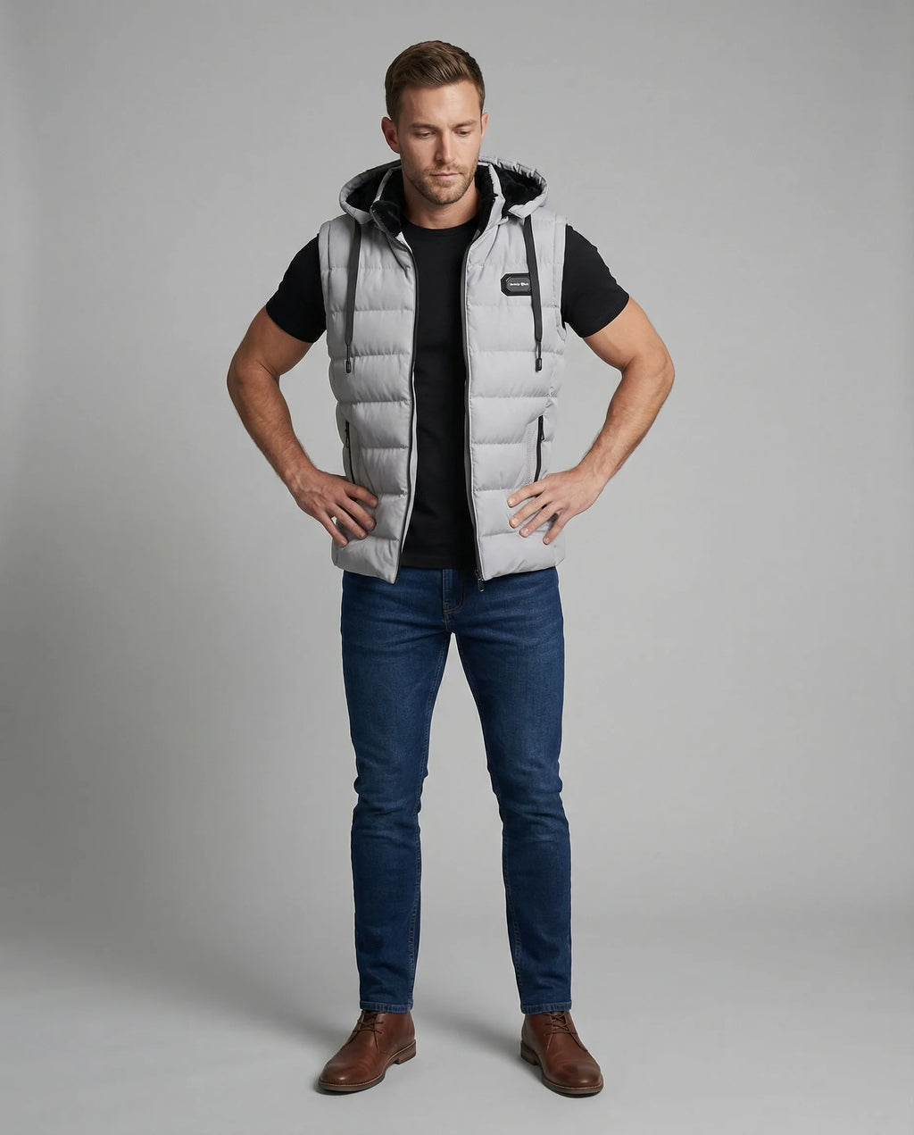 Full-length front view of a man styling a grey quilted gilet with a black t-shirt, jeans and brown boots