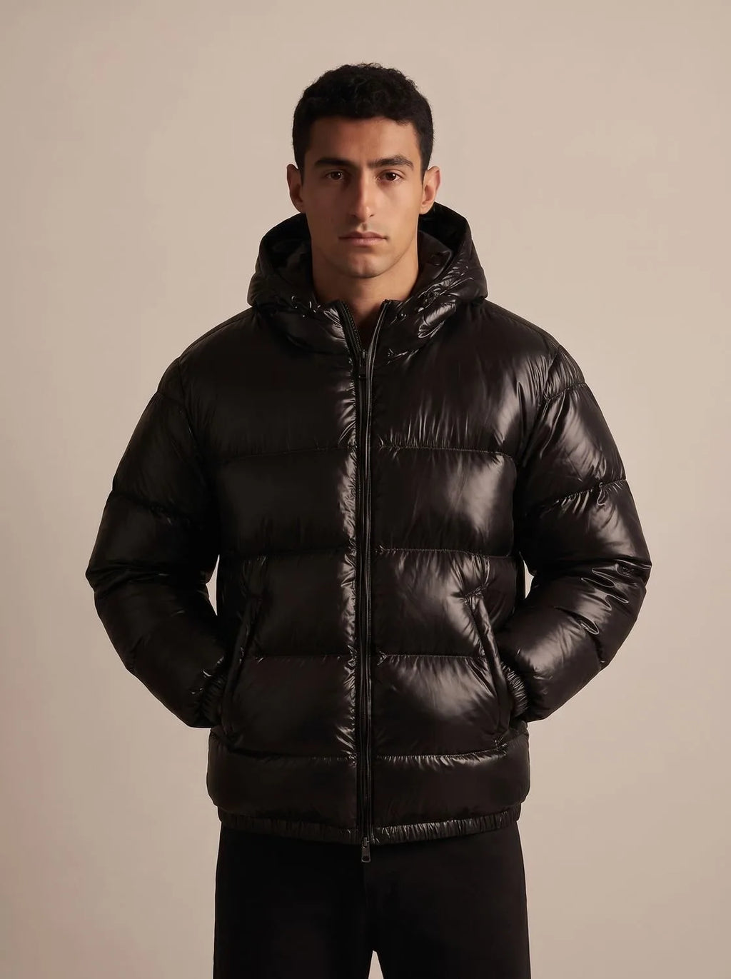 Man modelling the glossy black puffer jacket fully zipped up with the hood resting on his shoulders