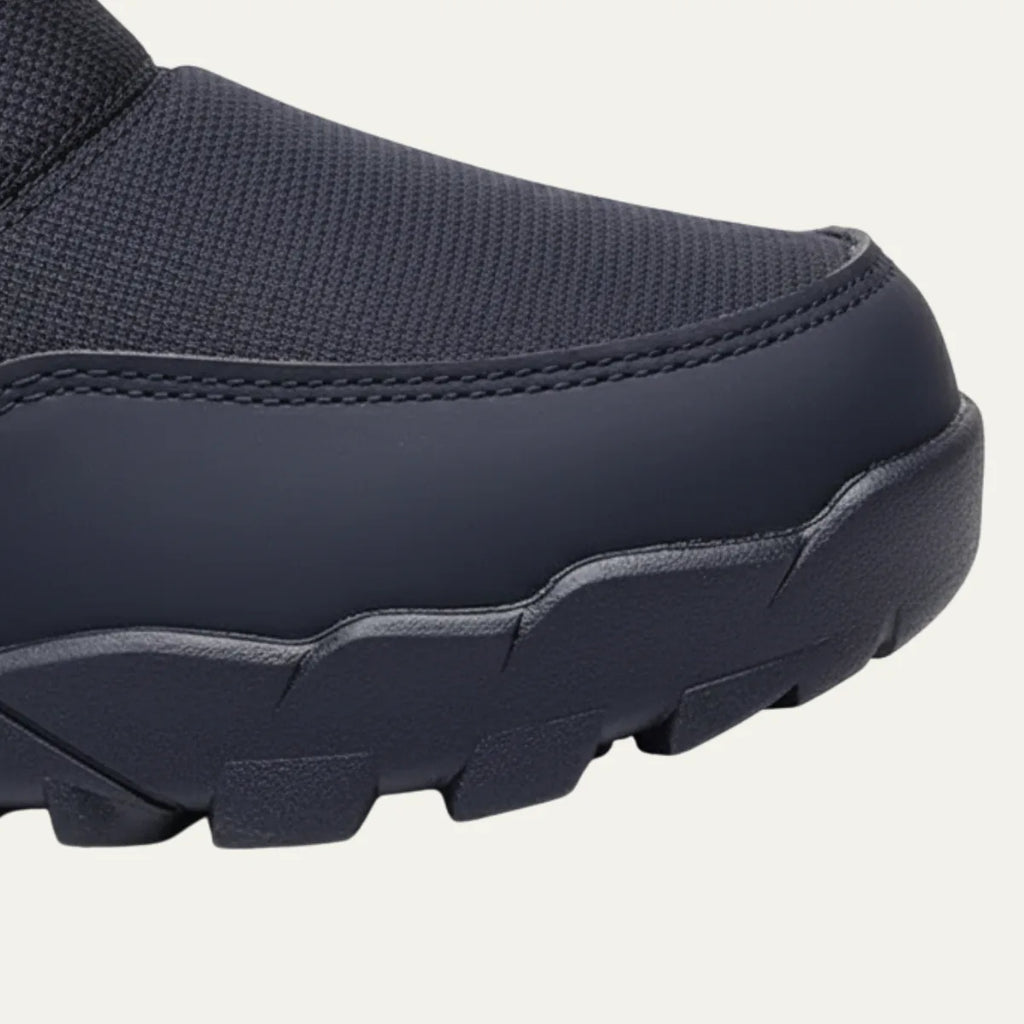 Close-up of the reinforced toe cap and deep-lug rubber outsole of a black snow boot