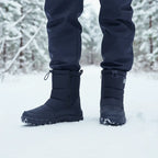 Person standing in snow wearing black insulated boots with visible snowflakes on the toe and sole