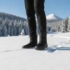 Close-up of black snow boots leaving footprints in deep snow with mountains in the background