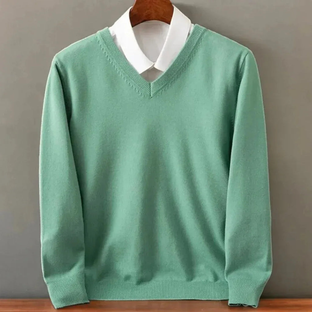 Sage green V-neck knit jumper styled over a crisp white collared shirt, front view on a hanger.
