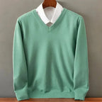 Sage green V-neck knit jumper styled over a crisp white collared shirt, front view on a hanger.