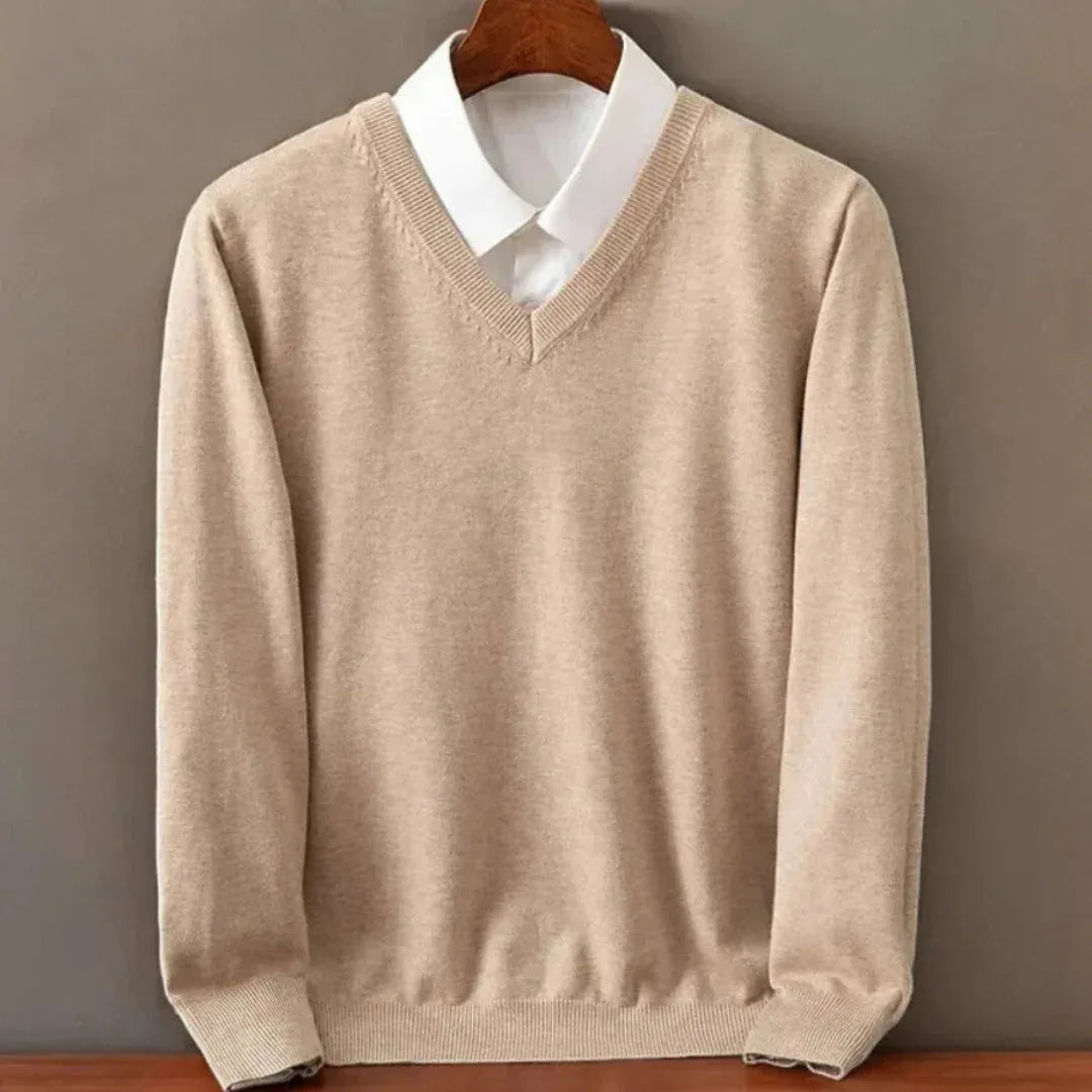 Beige V-neck jumper with white shirt collar peeking out, textured knit fabric visible in soft lighting.