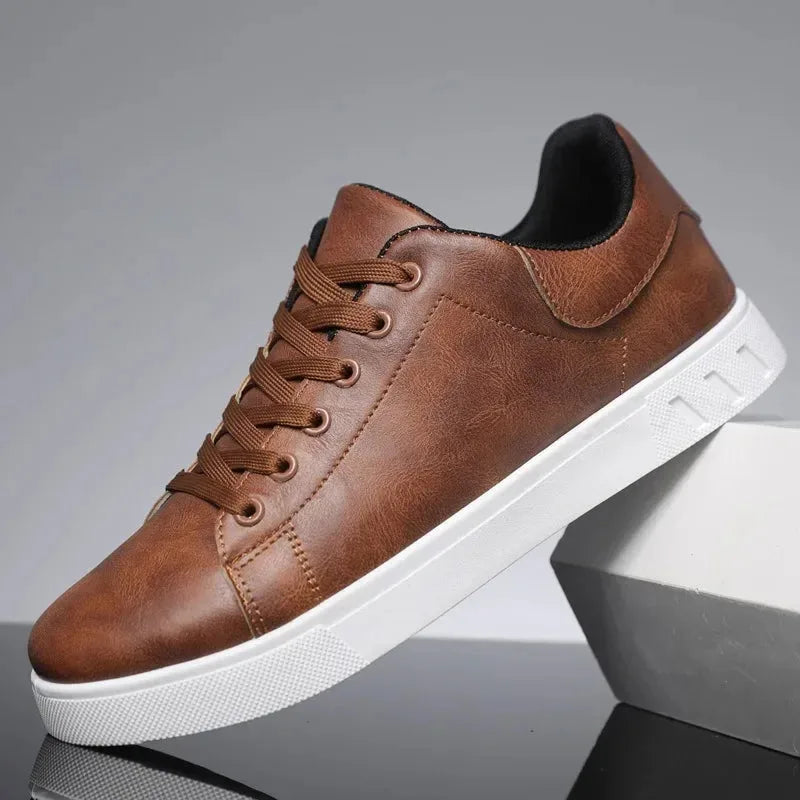 Side view of a brown leather lace-up trainer with tonal stitching, dark laces and a white sole, resting against a grey block.