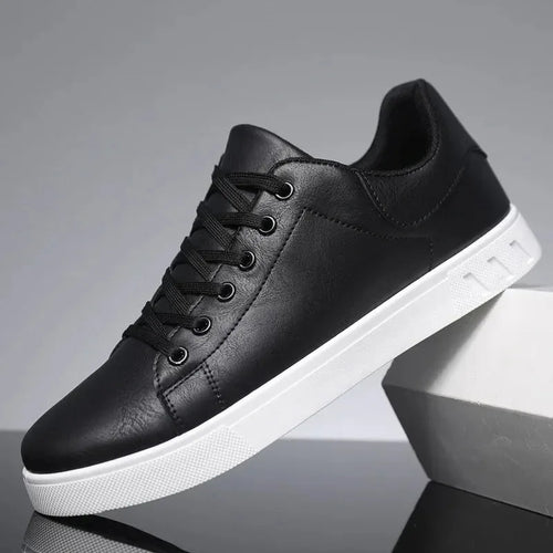 Side view of a black leather lace-up trainer with a padded ankle collar, black laces and a white sole, resting against a grey block.