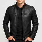 Black leather biker jacket with stand collar, snap button and chest zip pockets, hands resting in trouser pockets