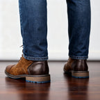 Rear view of a man wearing two pairs of brown leather combat boots with jeans, showing tread and heel