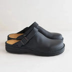 Side profile of matte black leather clog mules showing the buckle strap and chunky black outsole