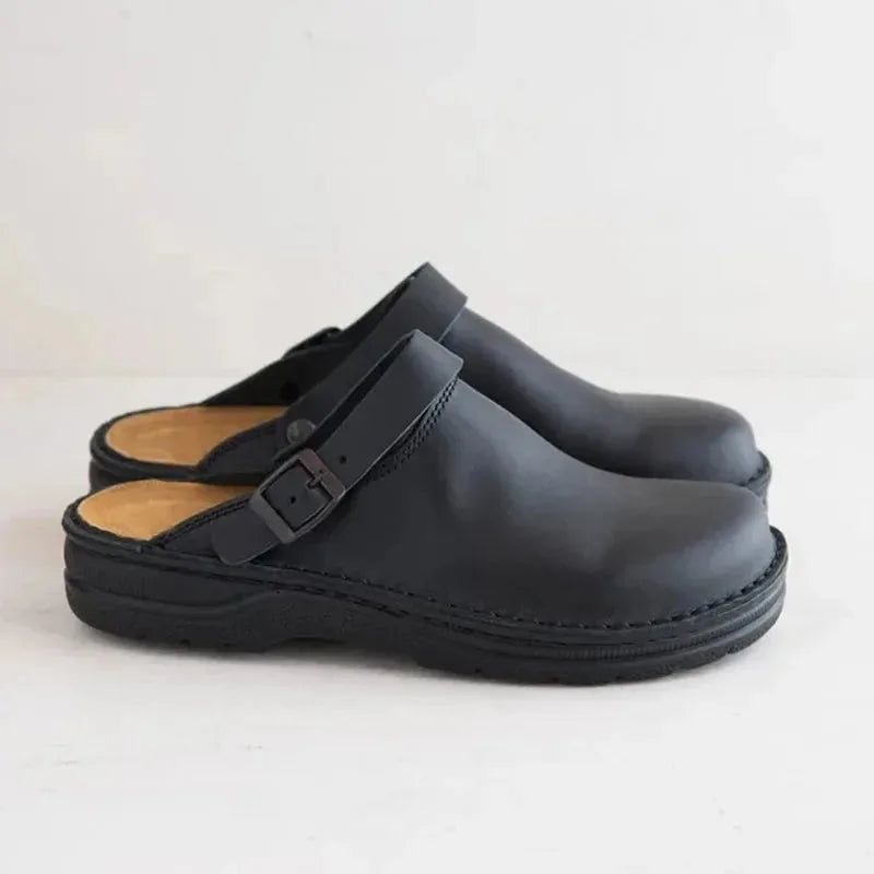 Side profile of matte black leather clog mules showing the buckle strap and chunky black outsole