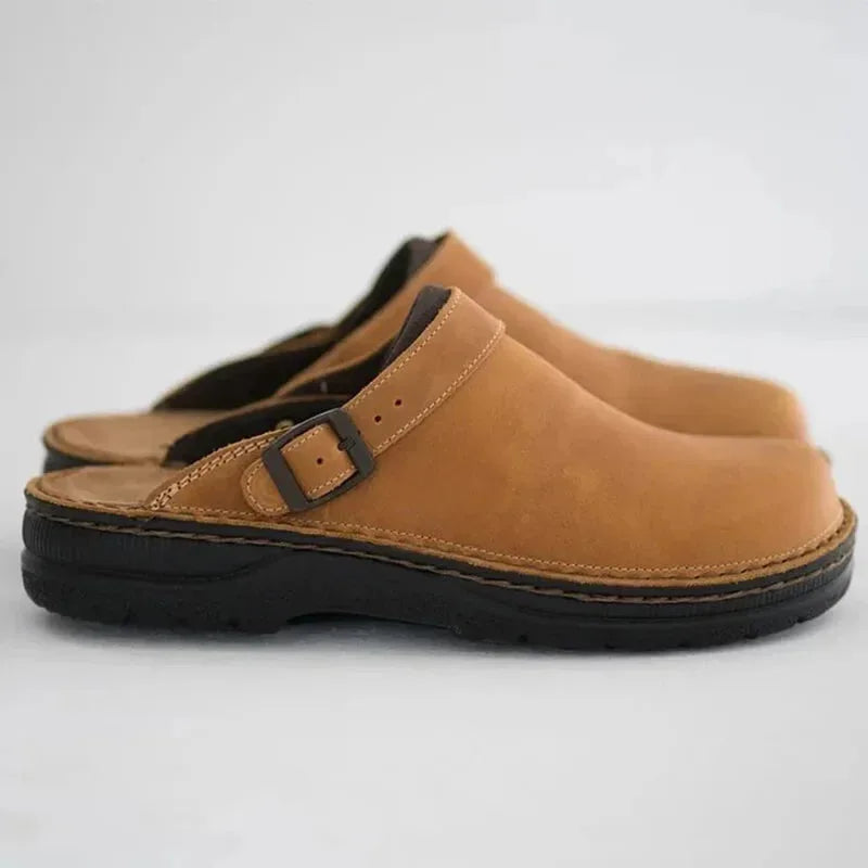 Side view of tan leather clog mules with a buckle strap detail and contrasting dark trim at the heel