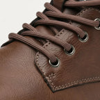 Macro shot of brown laces threaded through metal eyelets on leather upper