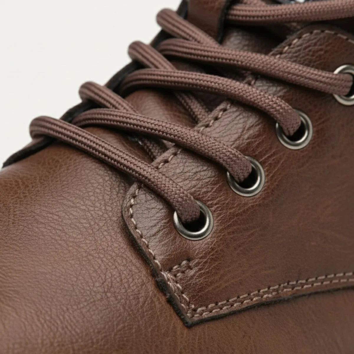 Macro shot of brown laces threaded through metal eyelets on leather upper