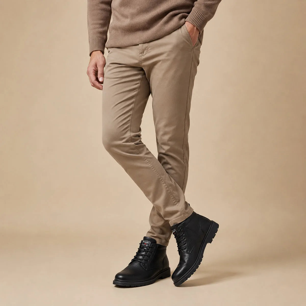 Man in taupe trousers wearing black lace-up leather ankle boots, side view