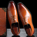Close-up side view of tan brown leather Derby dress shoes with cap-toe stitching and lace-up front, paired with a crocodile-embossed box
