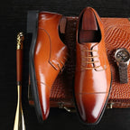 Overhead flat lay of tan brown lace-up leather dress shoes resting on a crocodile-textured case beside a wristwatch and shoehorn