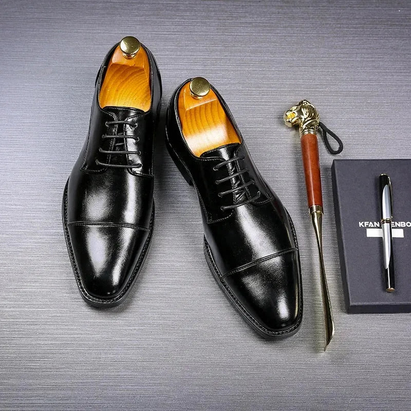 Pair of polished black leather lace-up dress shoes with wooden shoe trees, shown beside a pen and gift box