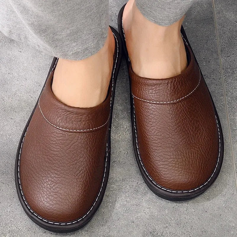 Top-down view of brown leather mule slippers worn barefoot, showing contrast white stitching and padded collar