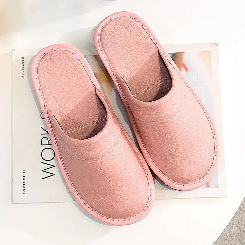 Front view of black leather slippers worn on bare feet, showing the rounded closed toe and padded vamp