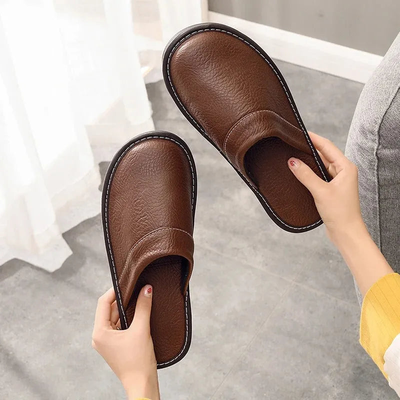 Close-up of a hand holding brown leather slippers, showing the soft insole and curved backless heel