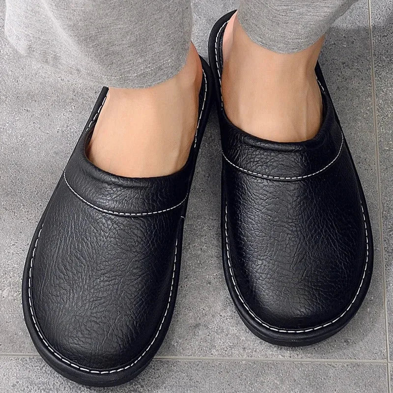 Top-down view of black leather mule slippers worn barefoot, showing white stitched trim around the opening