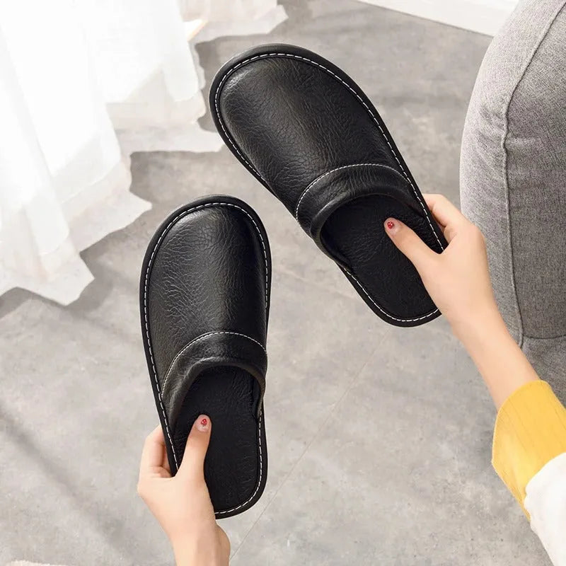 Close-up of a hand holding black leather slippers, showing the smooth insole and rounded toe shape