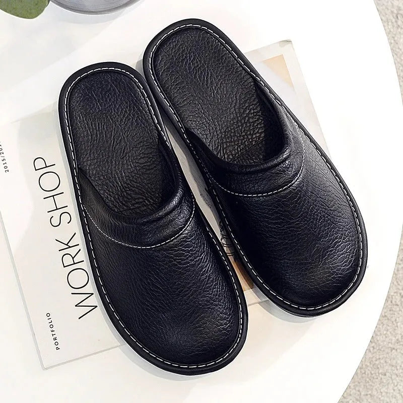 Overhead flat lay of a pair of black leather mule slippers on a white surface with a magazine beside them