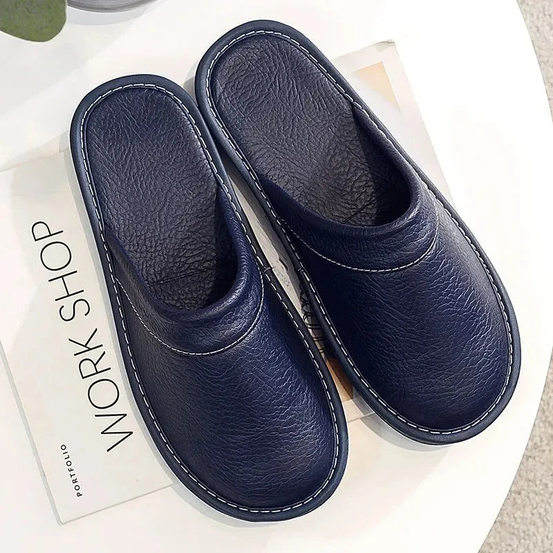 Overhead flat lay of a pair of navy leather mule slippers on a white surface with a magazine beside them